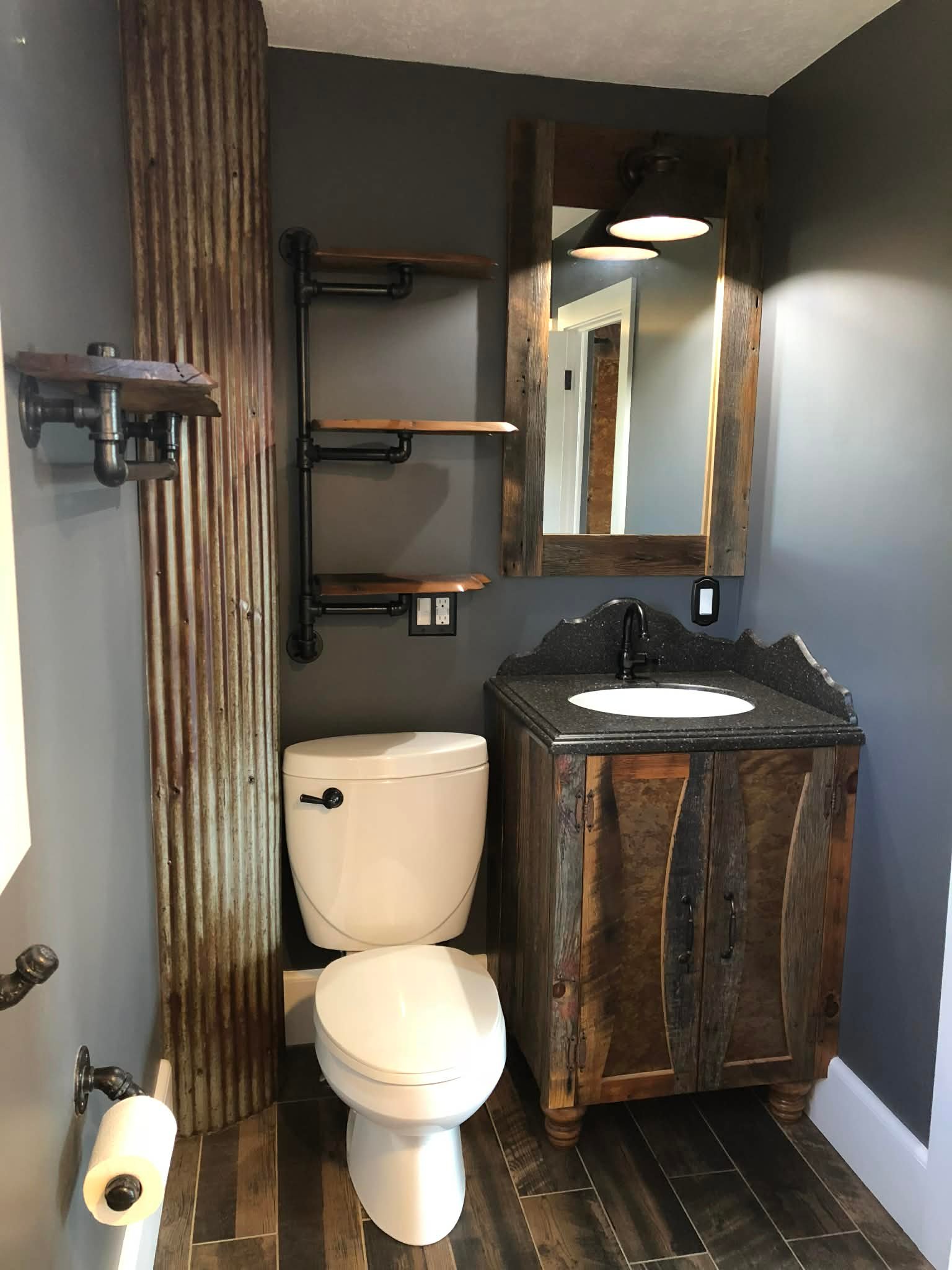 Rustic powder bath with custom vanity, framed mirror, and pipe shelving